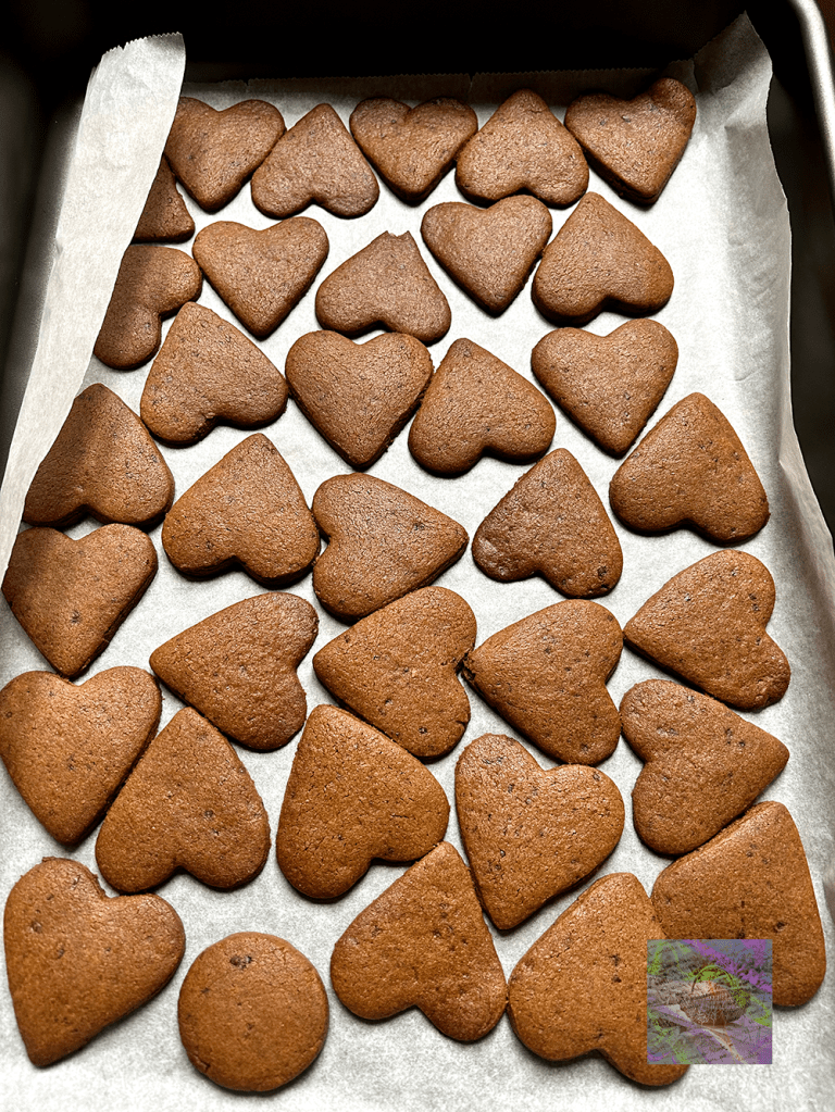 Ett bakplåt med hjärtformade pepparkakor i bruna nyanser, placerade på bakpapper.