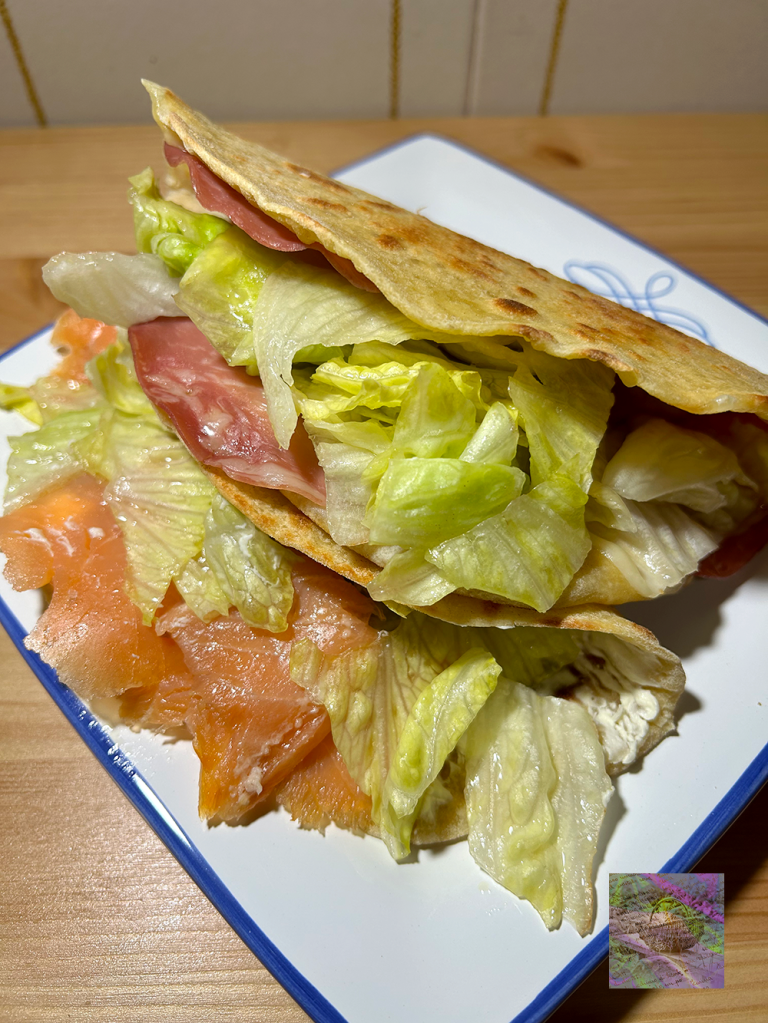 Close-up of a sandwich with layers of lettuce, ham, and smoked salmon, served on a blue-edged plate.